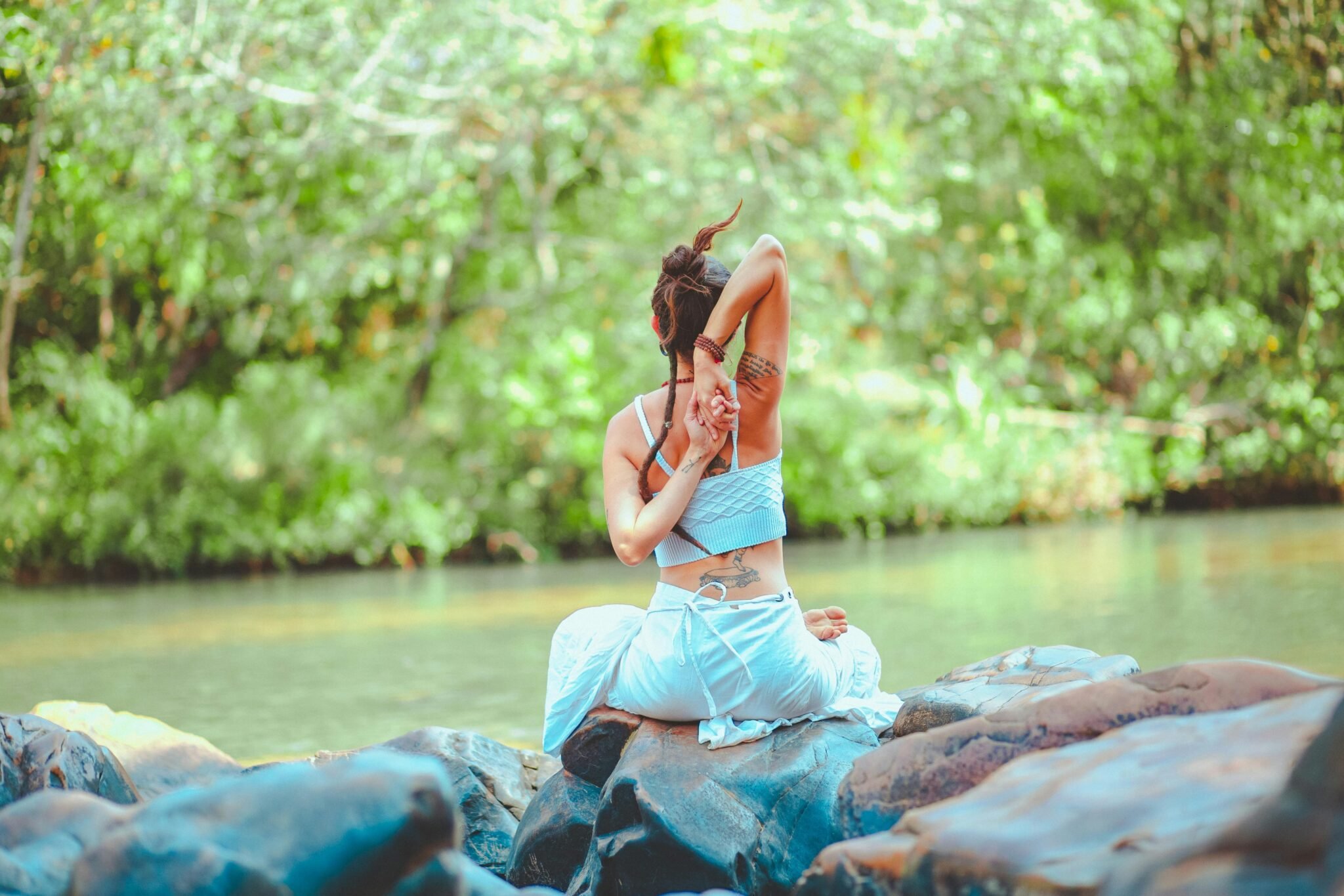 A woman meditating in nature, surrounded by lush greenery.